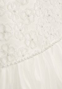 Weißes Kleid mit floraler Spitzenapplikation und Perlenakzenten. Der Tüllsaum sorgt für Textur, mit einem perlenbesetzten Taillenband als Detail.