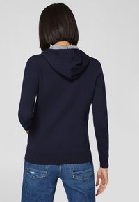 Marineblauwe hoodie met een trekkoord capuchon, lange mouwen en geribbelde manchetten, gecombineerd met blauwe spijkerbroeken met achterzakken.