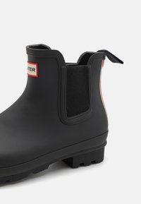 Μαύρη καουτσούκ μπότες μέχρι τον αστράγαλο με ελαστικά πάνελ και θηλιά. Διαθέτει υφή στη σόλα για πρόσφυση και πλακέτα λογότυπου κοντά στον αστράγαλο.