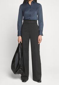 Camicia di raso blu scuro con bottoni frontali e maniche lunghe; pantaloni neri a vita alta con gamba larga; borsa in pelle nera con chiusura a cordoncino.