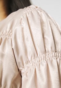 Ljusrosa blus tyg med en sidenliknande textur; har puffärmar och veckad detaljering vid sömmarna för en strukturerad look.