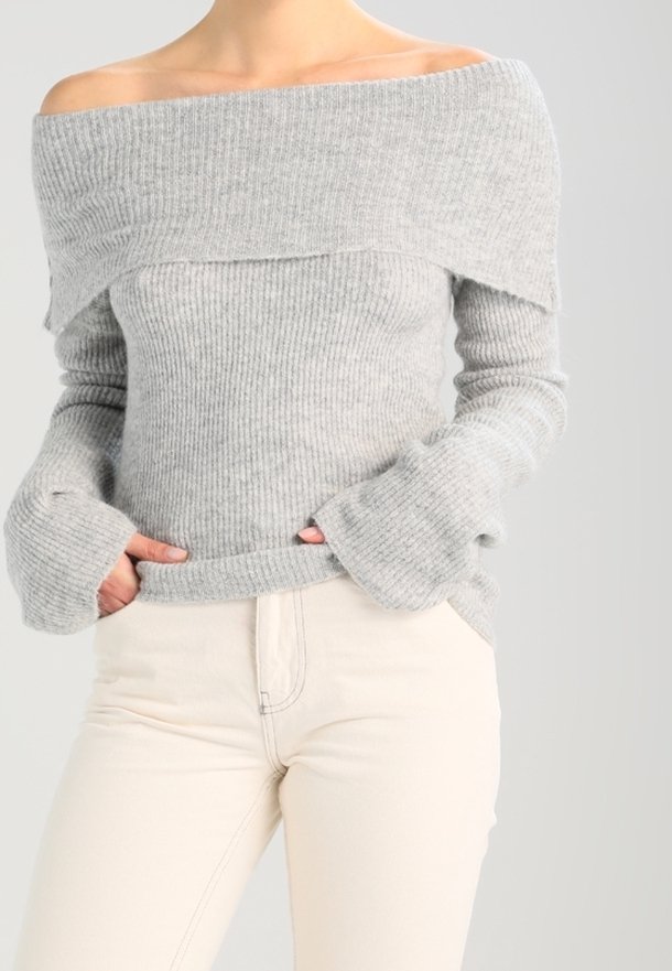 Pull en maille côtelée gris à col bateau avec manches larges, associé à un jean clair et ajusté. Détails de coutures visibles sur le jean.