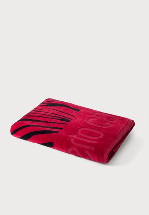 Gefaltetes rotes Handtuch mit schwarzem Tigerstreifenmuster und erhabenem Teiltext auf schlichtem weißem Hintergrund.