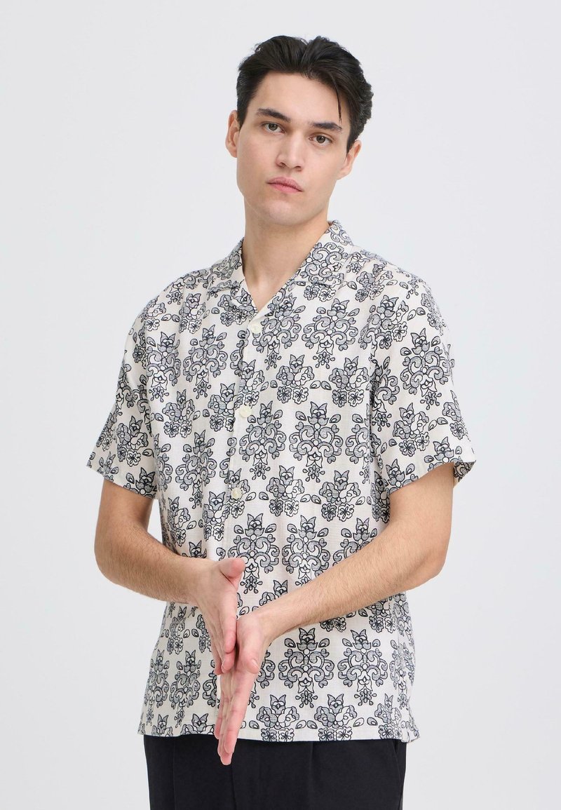 Korte mouwen blouse in lichtbeige met een zwart bloemenpatroon, voorzien van een kraag en knopen, gemaakt van geweven stof met een zachte textuur.