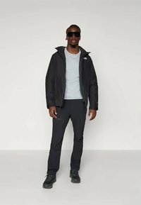 Μαύρο μόνωτο μπουφάν με κουκούλα, ανοιχτό μπλε πουκάμισο, μαύρο παντελόνι και μαύρα παπούτσια. Το μοντέλο φοράει γυαλιά ηλίου; το μπουφάν διαθέτει λογότυπο στο στήθος.