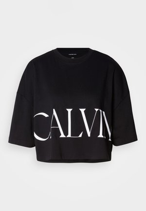 Black cropped t-shirt in cotton blend with wide sleeves. Features a bold white "CALVIN" logo across the front. Simple crew neckline.