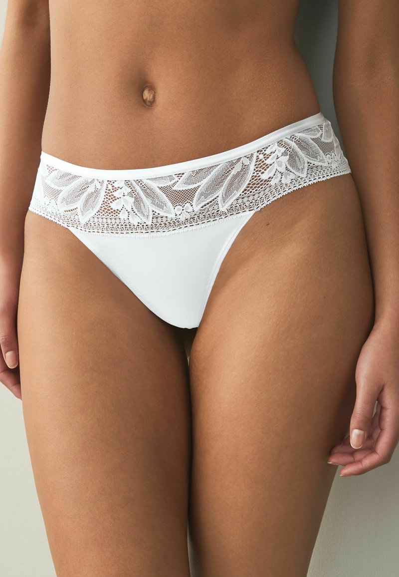 Culotte de bikini blanche avec une ceinture en dentelle à motifs floraux, texture douce et finition lisse. Les détails incluent une délicate bordure en dentelle.