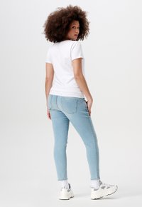 Witte t-shirt met korte mouwen in combinatie met lichtblauwe jeans. Model draagt witte sneakers met grijze accenten. Schoon, minimalistisch esthetiek.