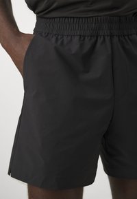 Pantalones cortos deportivos negros con una cintura elástica, textura suave, bolsillos laterales y un corte a la altura de la rodilla, que presentan pequeñas aberturas en el dobladillo.