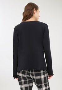 Maglietta nera a maniche lunghe con scollatura rotonda e orlo ondulato, abbinata a pantaloni a quadri bianchi e neri. Tessuto liscio.