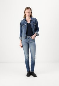 Denim jacket in medium blue with light blue jeans. Both have a faded look and distressed detailing. Plain black shoes complete the outfit.