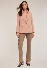 Blush roze dubbelbreasted blazer met een notch-kraag, gecombineerd met beige broeken en zwarte blokhak sandalen.