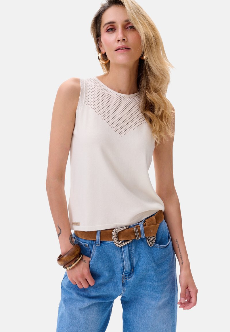 Crème mouwloos topje met een textuur in een ruitpatroon bij de halslijn, gecombineerd met lichtblauwe hoge taille jeans en een bruine riem.
