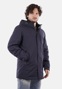 Giacca isolante blu navy con cappuccio, chiusura a zip e tasche laterali. Tessuto liscio, design moderno, adatta per l'uso all'aperto.