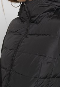 Black puffer jacket with a high collar, zip closure, and quilted sections. Smooth texture, lightweight, suitable for cold weather.