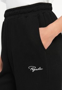 Čierne rebrované nohavice s elastickým pásom a bočnými vreckami. Na prednej strane majú biele vyšívané logo "Pegador".