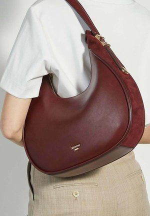 Donker bordeauxleren tas met een gladde textuur en een gebogen silhouet. Beschikt over gouden hardware en een schouderband voor gemakkelijk dragen.
