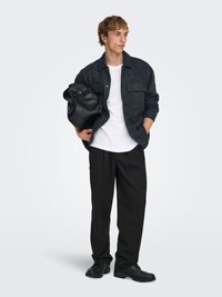 Veste-chemise en daim noir avec deux poches poitrine, t-shirt blanc, pantalon noir et chaussures noires. Porte un sac noir. Design simple.