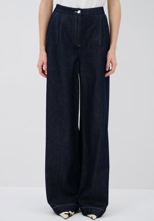 Wide-leg dark denim pants with a high waistband, front pleats, and a single button closure. Features white stitching and cuffed hems.