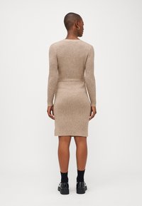 Strikket beige kjole med lange ermer og en tett passform. Har ribbestruktur og en kneveis hem. Kombinert med svarte klumpete sko.
