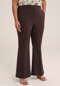 Pantalones de campana marrones con una textura suave, bolsillos frontales y una cintura de altura media. Combinados con sandalias de tiras ligeras.