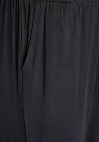 Zwarte stoffen broek met een relaxte fit, elastische tailleband en zijzakken. De textuur is glad en heeft een lichte uitstraling.