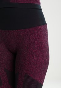 Leggings de cintura alta hechas de tela de punto en rosa oscuro con un patrón texturizado y una banda elástica negra acanalada. Presentan acentos de franjas oscuras.