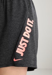 Tmavě šedé šortky s růžovým textem "JUST DO IT." a logem Nike swoosh na boku nad kolenem.