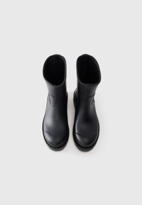 Une paire de bottes en caoutchouc noir mat avec des orteils ronds et une hauteur mi-mollet, présentée de dessus sur un fond blanc.