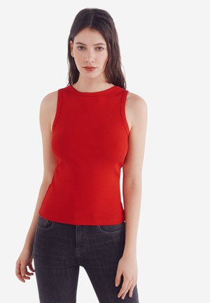 Rotes, geripptes, ärmelloses Oberteil mit rundem Ausschnitt. Hat eine figurnahe Passform, hergestellt aus elastischem Stoff. Kombiniert mit dunklen, geraden Jeans.