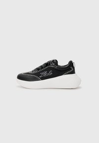 Basket noire avec semelle blanche, fabriquée en cuir et tissu. Présente des coutures contrastées et un logo sur le côté. Talon légèrement rehaussé.