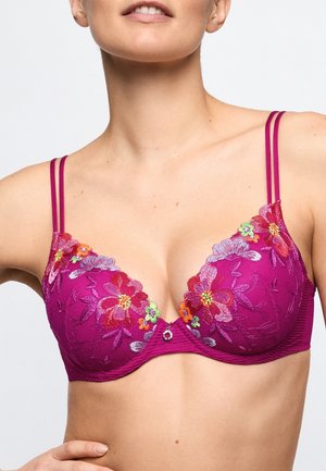 Vrouw die een paarse beha draagt met rood, roze, oranje en groen bloemrijk borduurwerk en dubbele schouderbandjes.