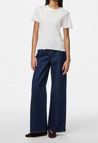 Vit ribbad kortärmad topp med vågiga kanter, kombinerad med vida mörk denimjeans. Skorna är mörkbruna med spetsig tå.