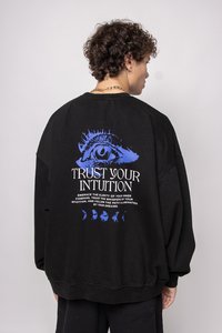 Sudadera oversize negra con un diseño gráfico de un ojo azul y texto blanco que dice "Confía en tu intuición" en la parte posterior; textura suave.