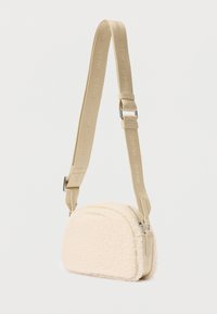 Bolso cruzado pequeño de color crema con una textura esponjosa y correa gruesa ajustable, embellecido con el nombre de la marca "HUGO".