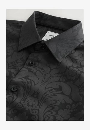 Camicia nera con una texture a fantasia che presenta design floreali e astratti, colletto classico e bottoni neri. Etichetta visibile all'interno del colletto.