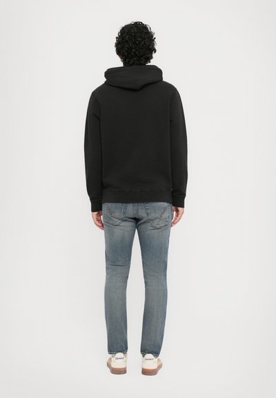 Zwarte hoodie met een kangoeroezak, gecombineerd met lichte, slim-fit jeans en beige sneakers met een gestructureerde zool.