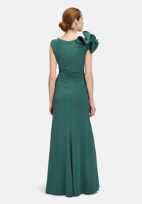 Robe longue verte avec un corsage ajusté et une jupe évasée. Elle présente des manches bouffantes avec des volants et une fermeture éclair discrète à l'arrière. Texture lisse.