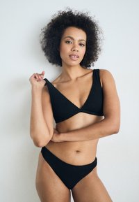 Czarny zestaw bikini wykonany z dzianiny z topem w kształcie litery V oraz szerokimi ramiączkami, a także dopasowanymi dolnymi częściami o niskim stanie, prezentującymi teksturowany materiał.