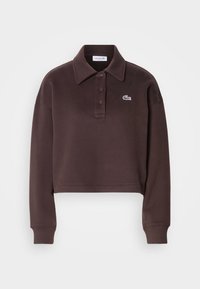 Cropped brown polo shirt in soft fabric, featuring a classic collar, three buttons, and a white Lacoste logo on the left chest.