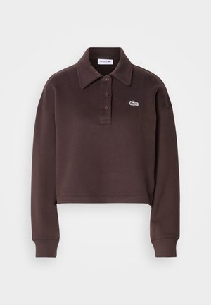 Beskåret brun polo skjorte i mykt stoff, med klassisk krage, tre knapper og en hvit Lacoste-logo på venstre bryst.
