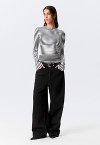 Sorte bukser med vide ben kombineret med en tætsiddende hvid og sortstribet bluse med lange ærmer. Outfit'et har et sort bælte og ærmer med vidde.