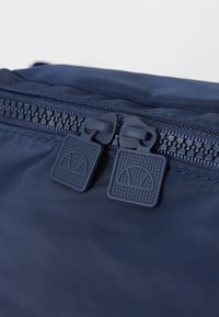 Borsa in nylon blu navy con una texture liscia, dotata di due zip scure, ognuna con un motivo a griglia e un design semicircolare.