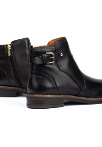 Bottines en cuir noir avec fermeture éclair sur le côté et détail de boucle. Présentent une texture lisse et un talon épais empilé. Doublure intérieure marron.