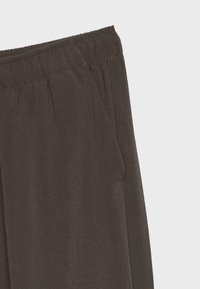 Pantalon gris foncé avec taille élastique et poche latérale, gros plan sur la partie haute de la hanche.