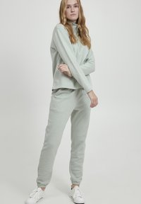 Ensemble de survêtement en polaire doux, gris clair, avec des manches longues, un col montant et un pantalon ajusté ; il comporte des poignets élastiques et des baskets blanches.