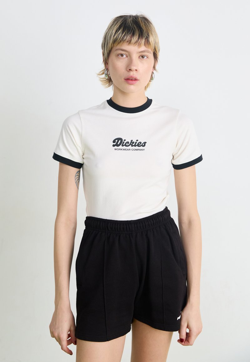 White short-sleeve shirt with black ringer details and "Dickies Workwear Company" logo. Worn with black elastic-waist shorts.