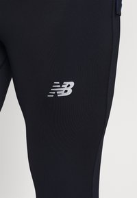 Leggings deportivos en azul marino con material elástico, que presentan un logo plateado de New Balance y costuras planas para mayor comodidad y ajuste.