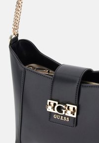 Zwarte neplederen handtas met een gouden hardware logo, kettingaccent riem en een opening met bovenrits. Getextureerde afwerking, slank design.