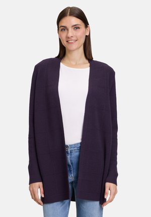 Lila gestrickte Strickjacke mit offenem Vorderteil, langen Ärmeln und einem strukturierten Karomuster, kombiniert mit einem weißen Oberteil und blauen Jeans.